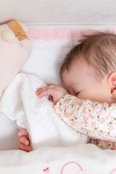 Baby sleeping in a cot with pacifier and toy covering her face