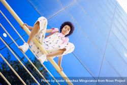 Low angle shot of woman sitting on handrails in front of  reflective building 0Plal0