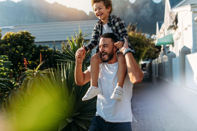 Happy man with his son sitting on his shoulders walking on street