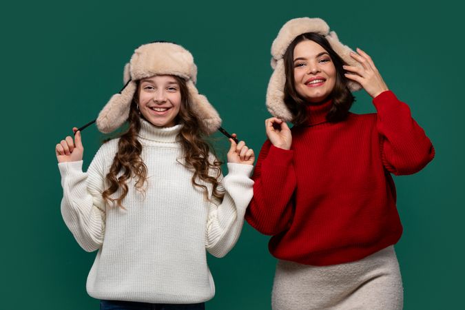Mum and teenage daughter wear furry winter hats, smiling