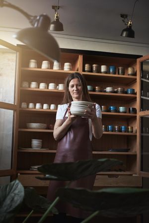 Woman in leather apron inspecting a stack of handmade plates in her rustic shop