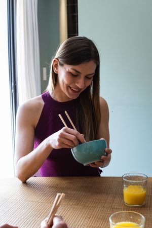Cheerful woman with chopsticks having lunch in dining room