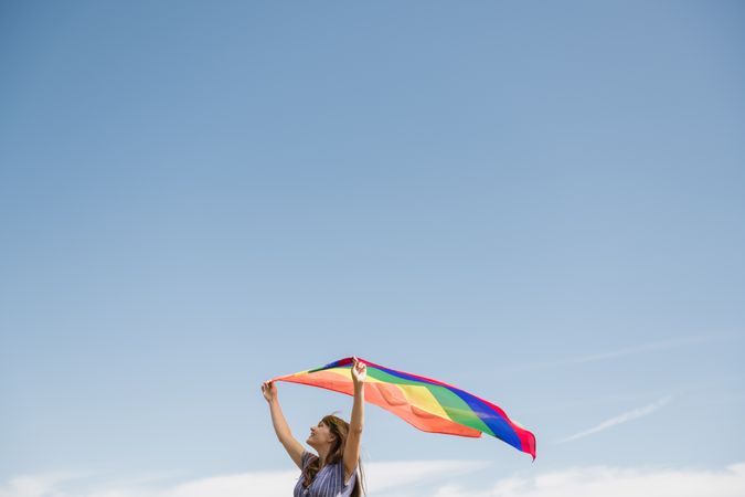 Young woman with rainbow banner against sky