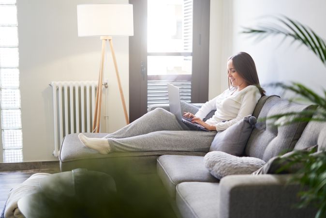 Smiling woman browsing on laptop and sitting on settee