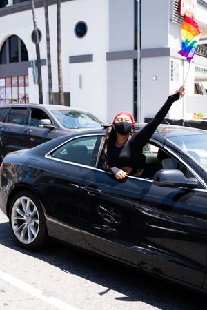 Los Angeles, CA, USA — June 14th, 2020: woman smiling at camera waving rainbow flag from car window