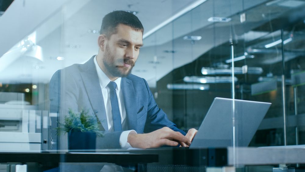 Confident Businessman Works on a Laptop at His Desk.
