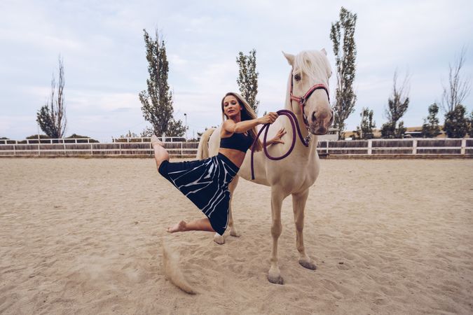 woman in skirt leaning on horse side while dancing at paddock