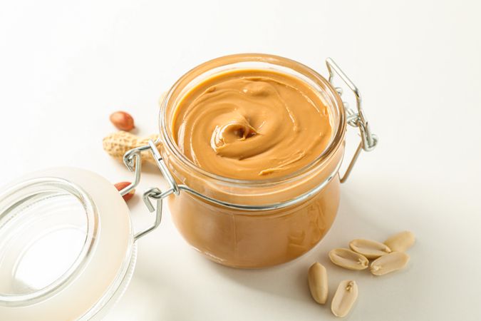 Composition with glass jar with peanut butter and peanut on light background, space for text and closeup