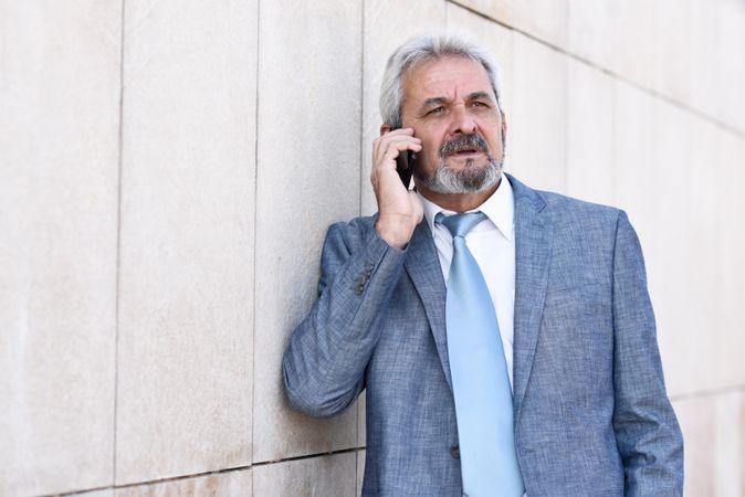 Grey haired male in formal suit talking on phone outside building