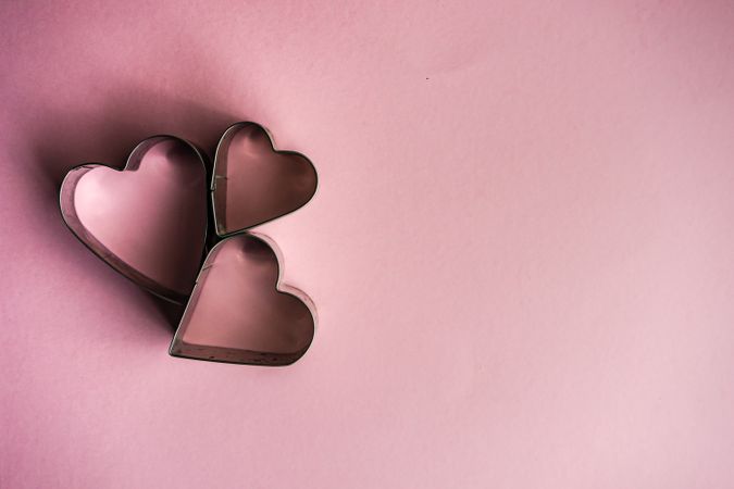 Three heart shaped cookie cutters on pink background