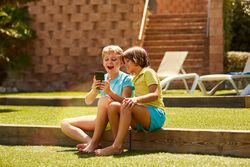Cheerful boys browsing smartphone sitting on garden