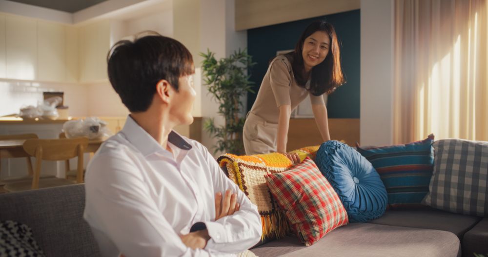Happy Homeowners Moving In: Lovely Korean Couple in their New Cozy Apartment Unpacking Boxes and Decorating the Sofa.