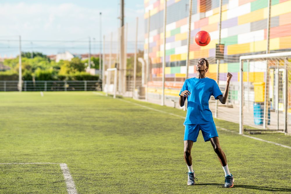 Black teenager jugging football ball on head