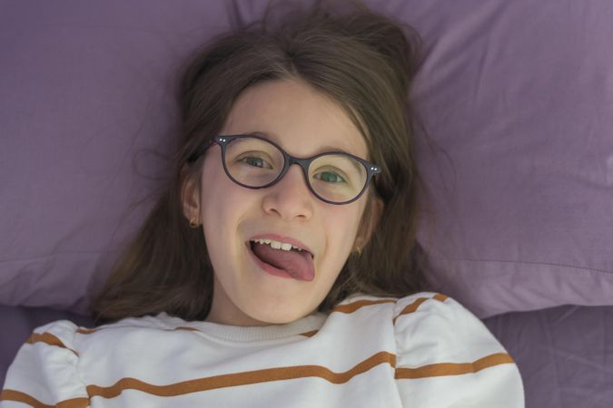 Girl wearing eyeglasses lying on bed