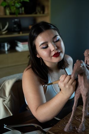 Young woman with classic makeup works on clay sculpture inside
