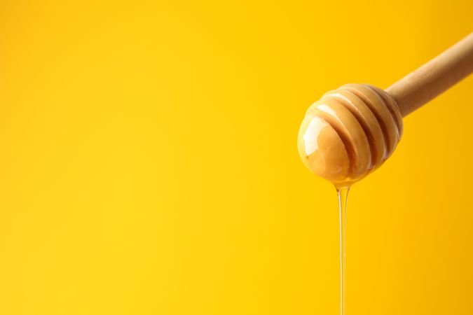 Dipper with honey on yellow background, space for text