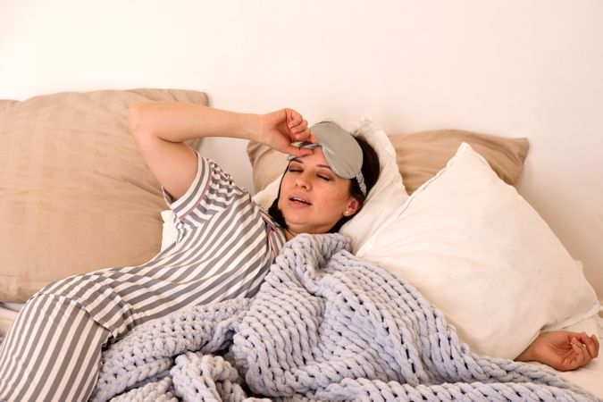 Woman waking up, adjusting eye mask in bed.