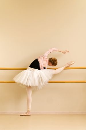 Ballerina performing deep leg stretch at barre during practice.