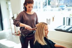 Hair stylist using heat tool on female client sitting in salon chair