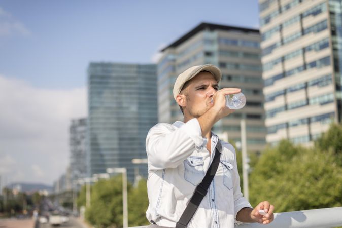 Relaxed male in denim with city in background drinking from water bottle
