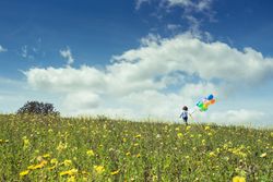 Unrecognizable child walking in grassy countryside with balloons