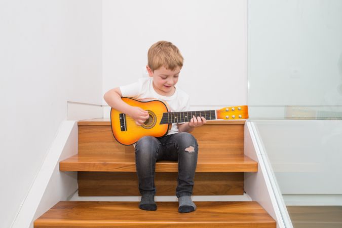 Young blonde boy playing toy guitar