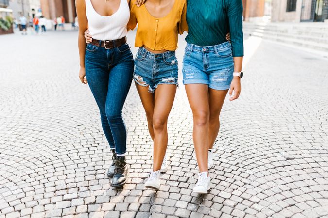 Legs of three female friends walking on cobbled street