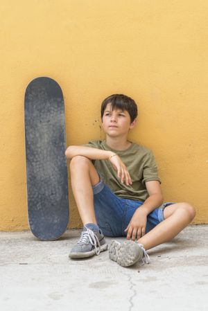 A serious boy with sitting skateboard alone
