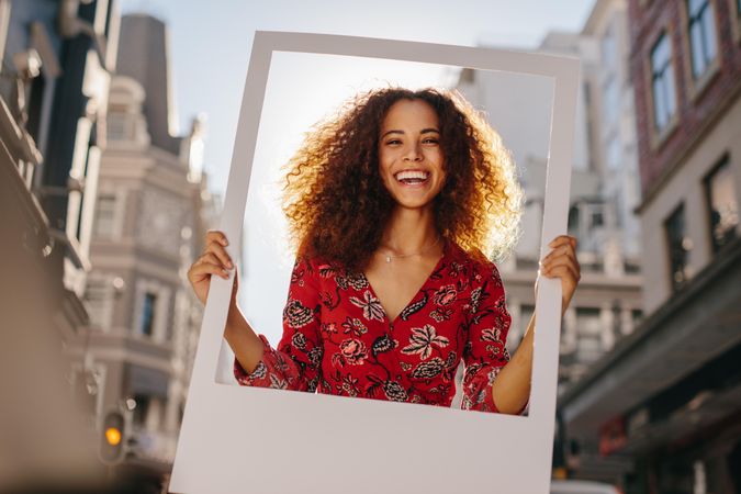 Joyful woman smiling while holding a polaroid photo frame around her face