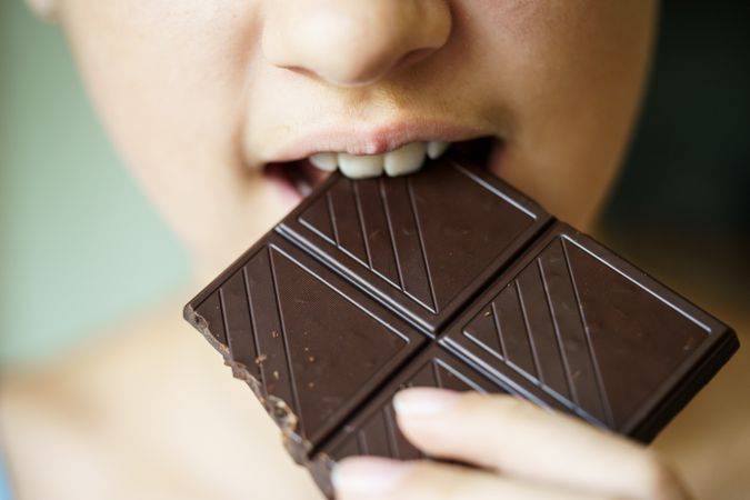 Unrecognizable young girl biting into delicious chocolate bar