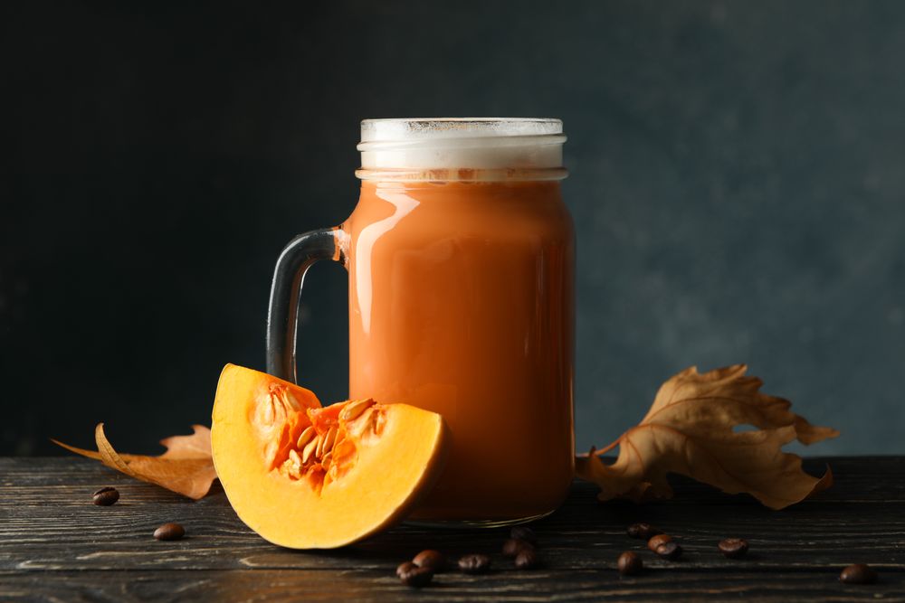 Glass jar of pumpkin latte, coffee seeds and leaves on wooden background
