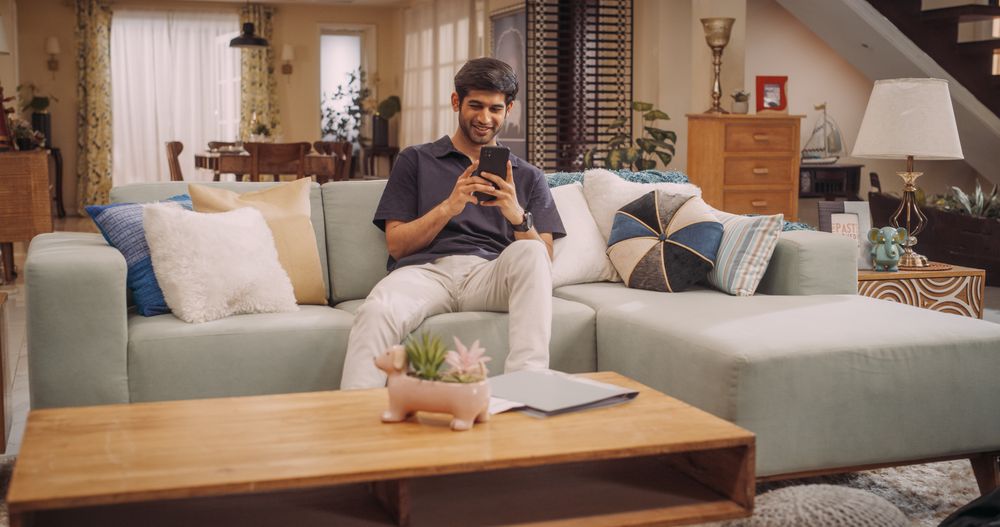 Indian Man Using Smartphone at Home: Seamlessly Managing Personal Finances, Exploring New Recipes