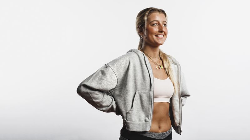 Portrait of smiling fitness woman standing against neutral background with hands on waist