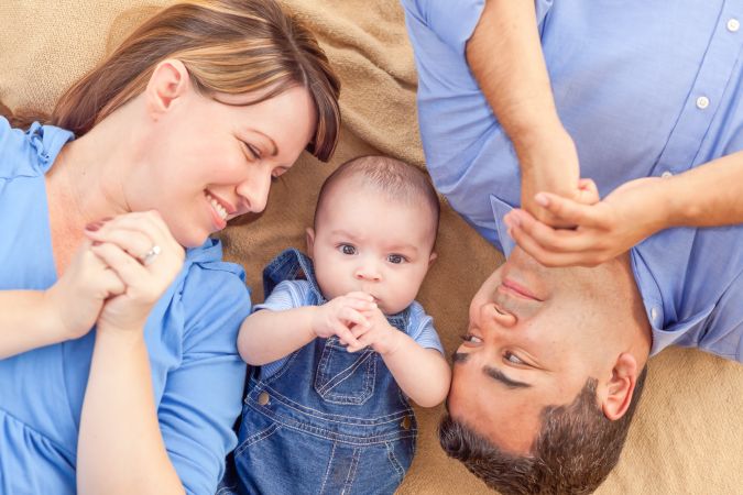 Young Couple Laying With Their Infant On A Blanket