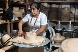 An adult Hispanic woman is cutting the brim of a natural fiber hat