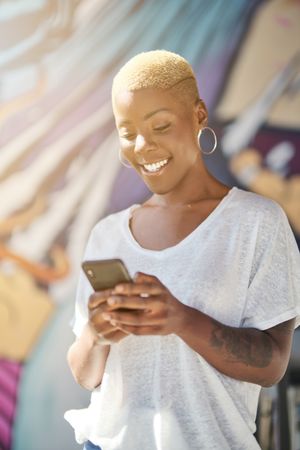 Cheerful Black female browsing smartphone against graffiti