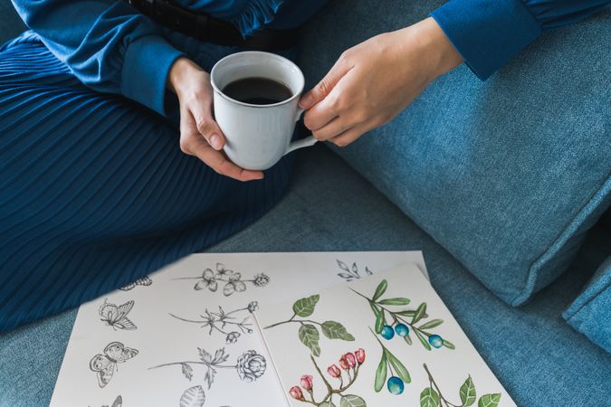 Young anonymous woman with coffee looking album with pictures