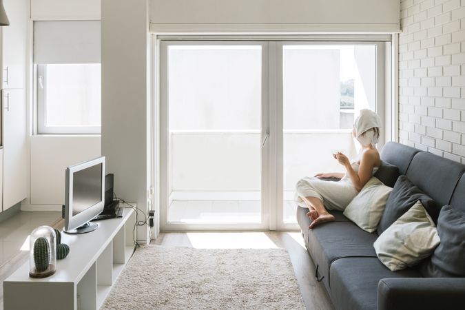 Adult relaxed woman enjoying life while resting on sofa and having hot drink after shower in own cozy apartment