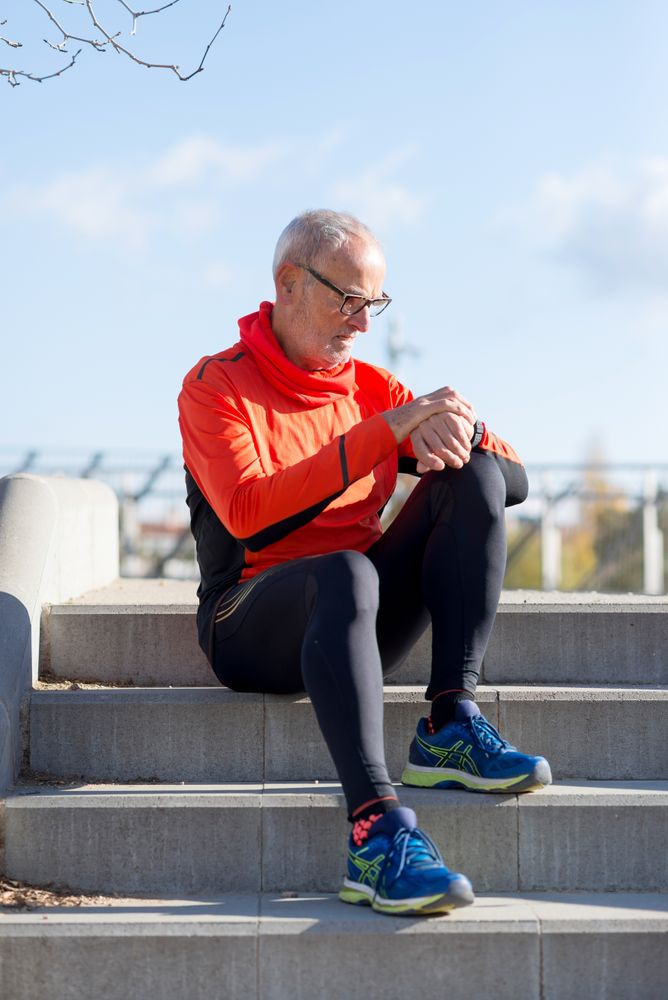 Male with grey hair checking watch sitting on steps outside