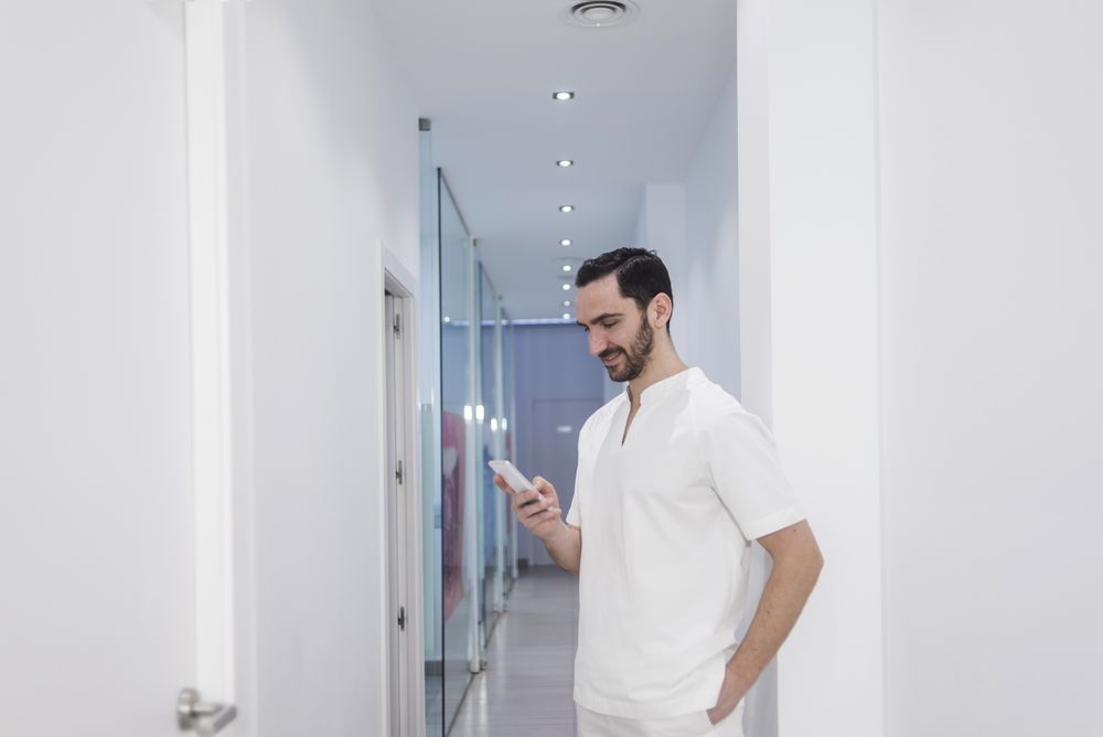 Bearded male medical professional smiling while using a smartphone at hospital