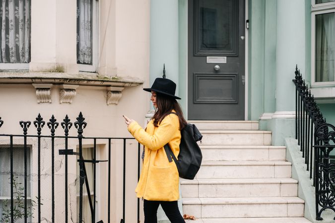 Stylish woman using smartphone near house on street