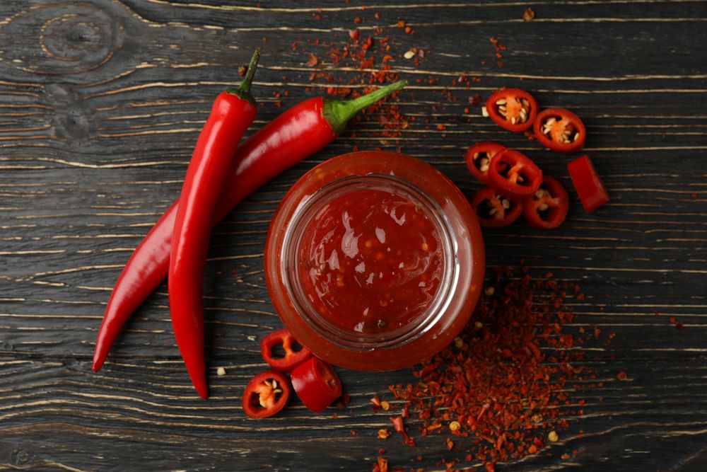Chilli pepper and glass jar of sauce on wooden  background, top view