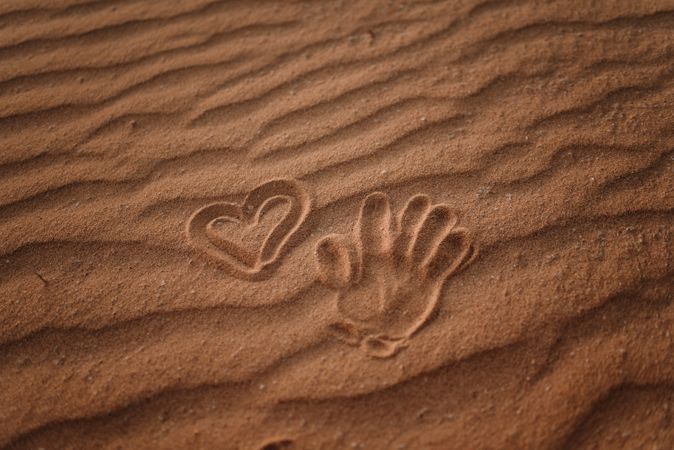 Heart drawn in sand and trace of palm on beach