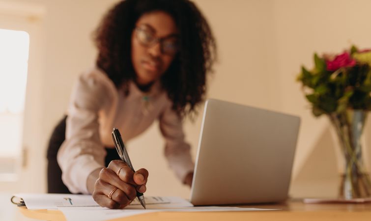 Businesswoman writing notes with a laptop open while working at home