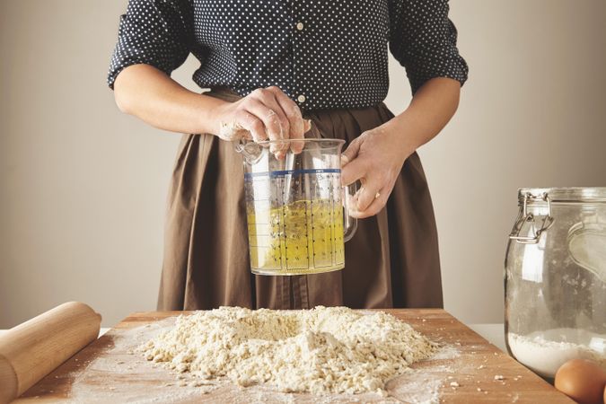Woman stirring oil and water in measuring cup over pile of dough