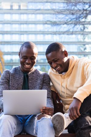 Smiling Black men using laptop while sitting on bench