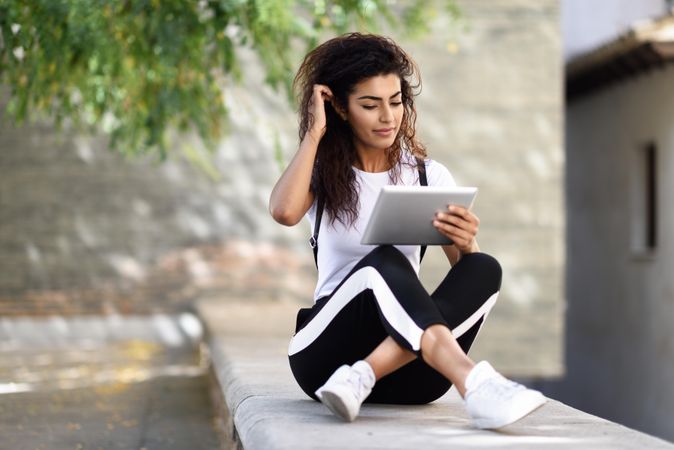 Arab woman looking down at her digital tablet while sitting outdoors