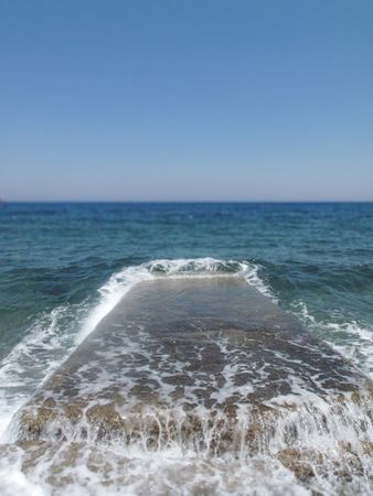 Seawater washes over broken stone jetty at Lampi beach, Patmos