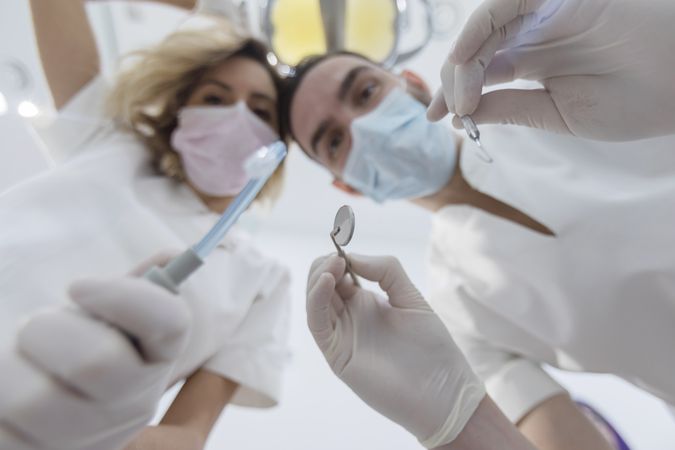 Dental colleagues wearing surgical mask while holding angled mirror and drill, ready to begin