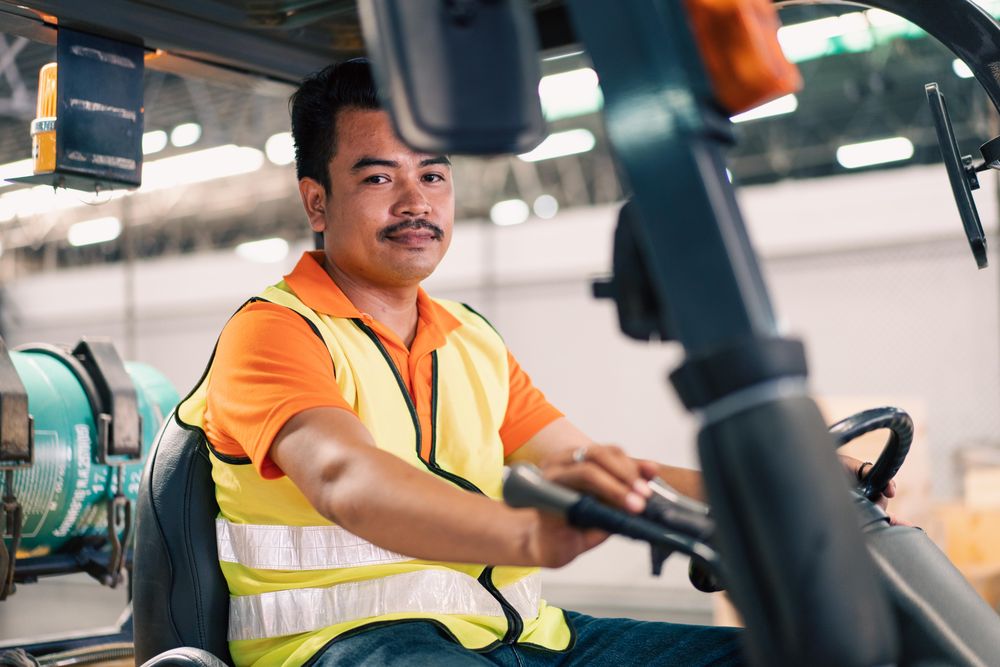 Man in high visibility vest driving forklift in warehouse